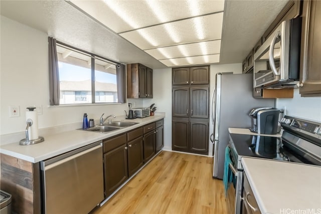 kitchen with a textured ceiling, sink, light hardwood / wood-style floors, dark brown cabinetry, and stainless steel appliances