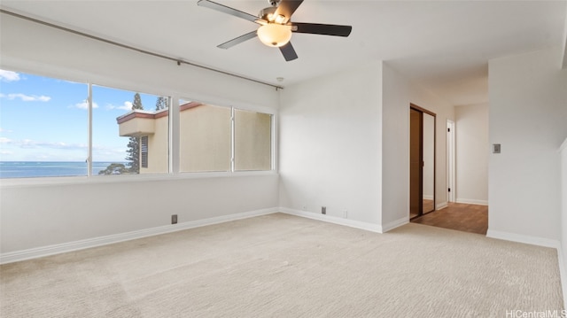 empty room featuring light carpet, a water view, and ceiling fan