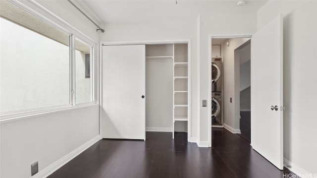 unfurnished bedroom featuring a closet, stacked washer and dryer, and dark hardwood / wood-style floors