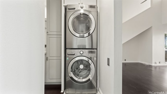 clothes washing area with cabinets, stacked washer / drying machine, and dark wood-type flooring