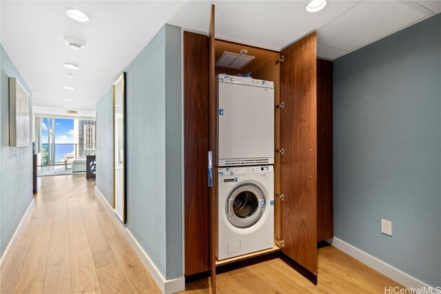 clothes washing area with light hardwood / wood-style flooring and stacked washer and dryer