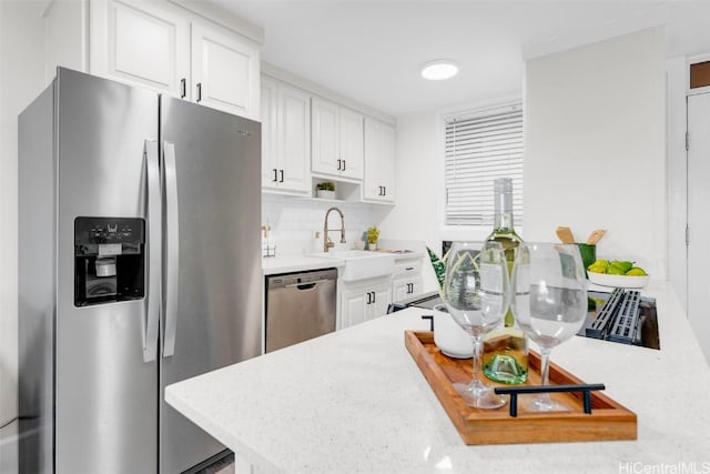 kitchen with appliances with stainless steel finishes, sink, white cabinets, backsplash, and light stone countertops