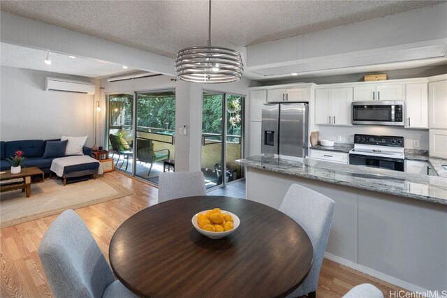 dining space featuring a wall mounted air conditioner, a textured ceiling, light hardwood / wood-style floors, and a chandelier