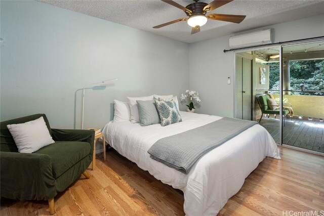 bedroom with ceiling fan, access to exterior, a textured ceiling, light hardwood / wood-style floors, and a wall unit AC