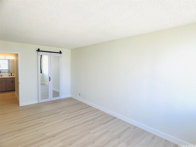 1255 Nuuanu Ave Unit E1414, Honolulu, HI 96817 - unfurnished bedroom featuring a barn door, light wood-type flooring, baseboards, and a textured ceiling