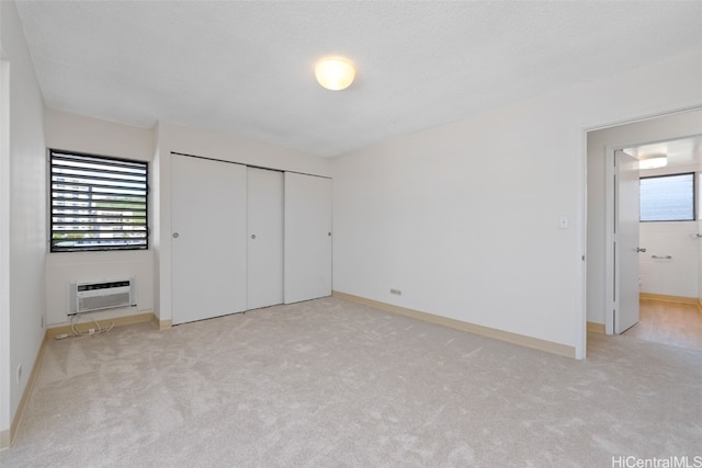 unfurnished bedroom featuring a closet, an AC wall unit, a textured ceiling, and light colored carpet