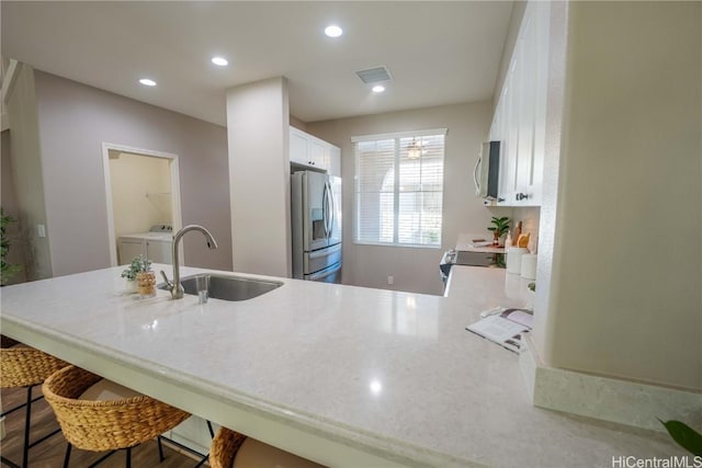 kitchen featuring appliances with stainless steel finishes, washer and clothes dryer, sink, white cabinets, and a breakfast bar area