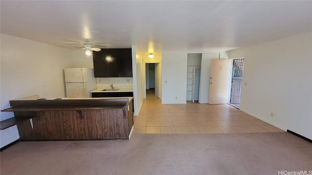 kitchen featuring sink, light tile patterned floors, ceiling fan, white refrigerator, and kitchen peninsula