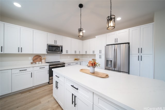 kitchen featuring appliances with stainless steel finishes, white cabinetry, light hardwood / wood-style flooring, and hanging light fixtures