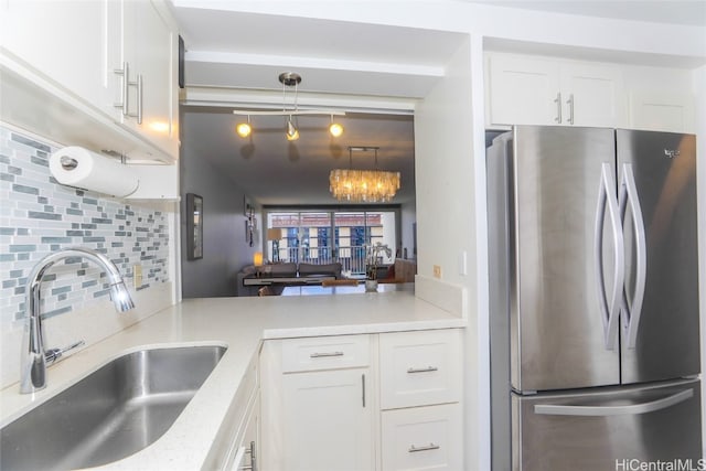 kitchen with hanging light fixtures, sink, white cabinetry, stainless steel refrigerator, and tasteful backsplash