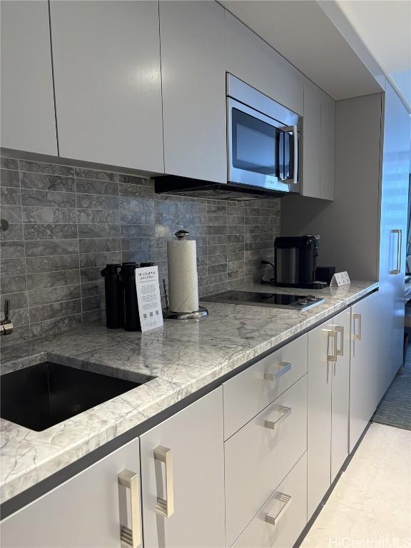 kitchen featuring white cabinetry, tasteful backsplash, light stone countertops, and black cooktop