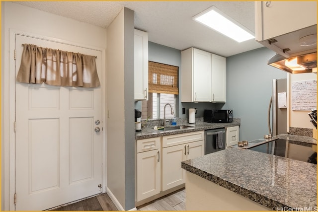 kitchen with appliances with stainless steel finishes, sink, light wood-type flooring, a textured ceiling, and white cabinets