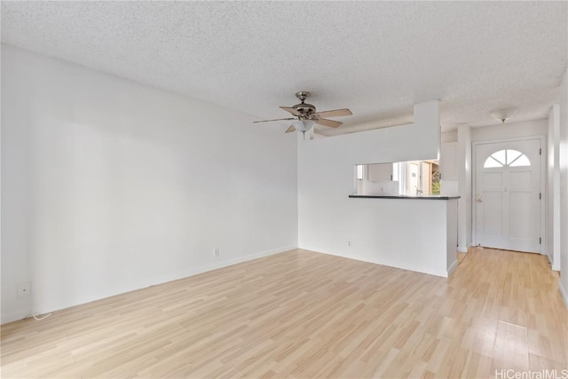 unfurnished living room with ceiling fan, a textured ceiling, and light wood-type flooring