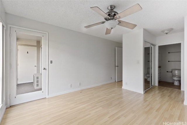 unfurnished bedroom with light wood-type flooring, a textured ceiling, ceiling fan, connected bathroom, and a closet