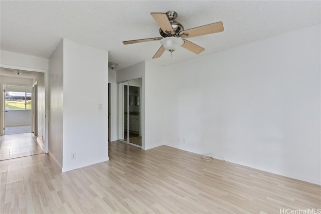 empty room with ceiling fan, light wood-type flooring, and a textured ceiling