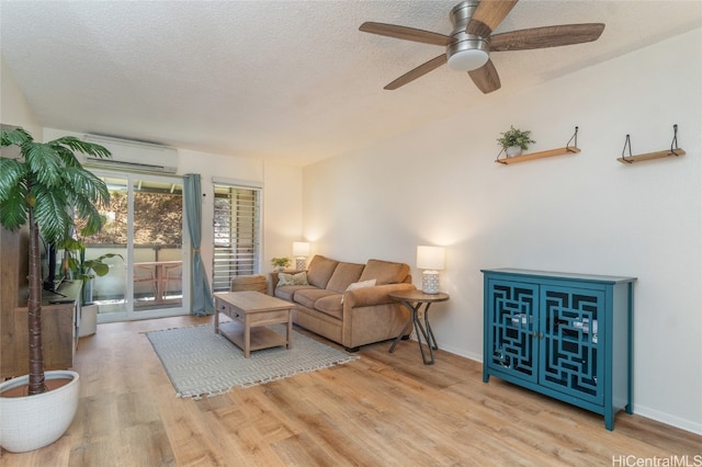 living room with ceiling fan, an AC wall unit, a textured ceiling, and light hardwood / wood-style flooring