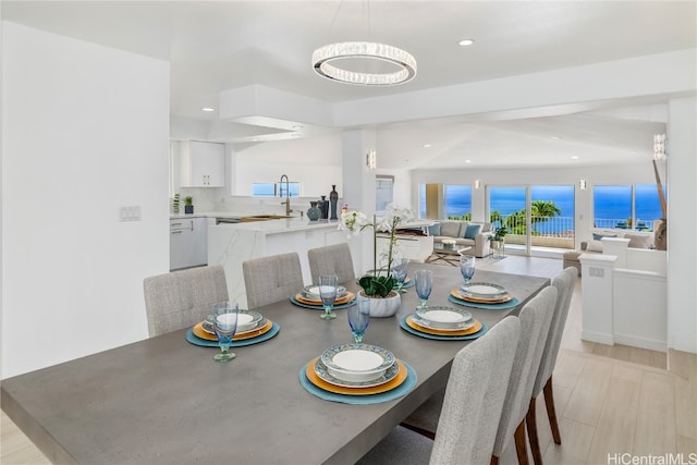 dining area with sink, a water view, a chandelier, and light wood-type flooring