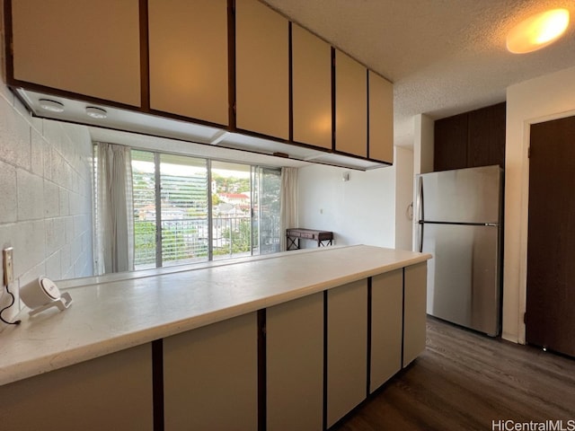 kitchen featuring dark hardwood / wood-style flooring, a textured ceiling, backsplash, and stainless steel refrigerator