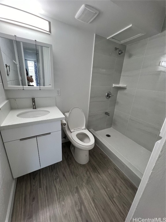 bathroom with vanity, toilet, wood-type flooring, and tiled shower