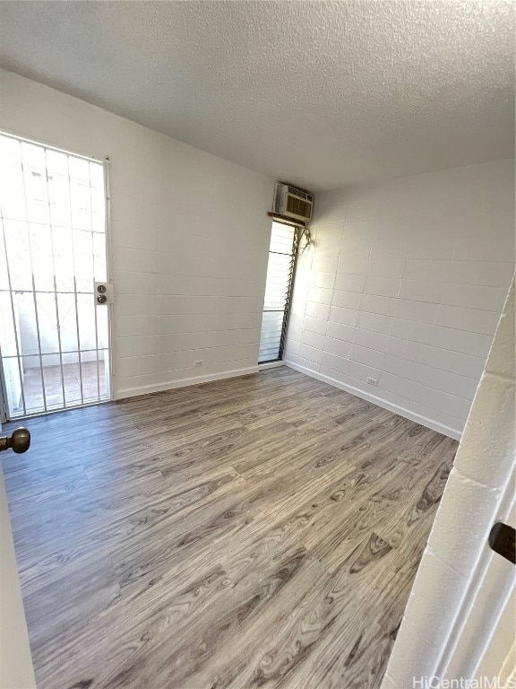 spare room with hardwood / wood-style floors, a wall unit AC, and a textured ceiling