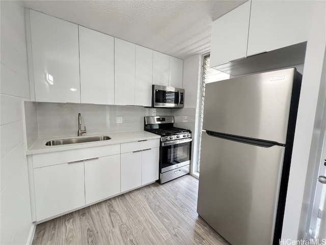 kitchen featuring appliances with stainless steel finishes, white cabinetry, a textured ceiling, light wood-type flooring, and sink