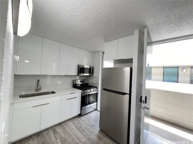 kitchen with light hardwood / wood-style flooring, stainless steel appliances, sink, white cabinetry, and a textured ceiling