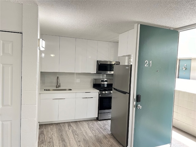 kitchen featuring white cabinets, backsplash, appliances with stainless steel finishes, light hardwood / wood-style flooring, and sink