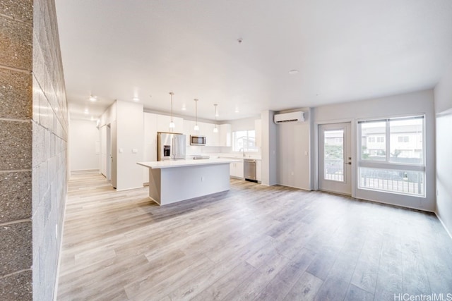 kitchen with appliances with stainless steel finishes, a wall mounted air conditioner, a kitchen island, white cabinetry, and decorative light fixtures