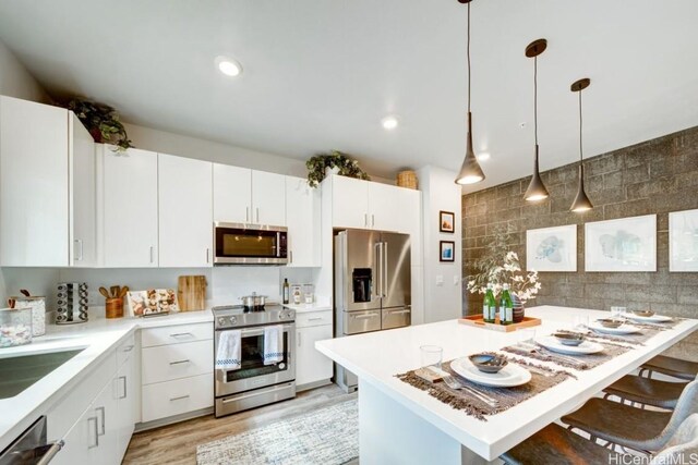 kitchen featuring hanging light fixtures, a kitchen breakfast bar, a kitchen island, stainless steel appliances, and white cabinets