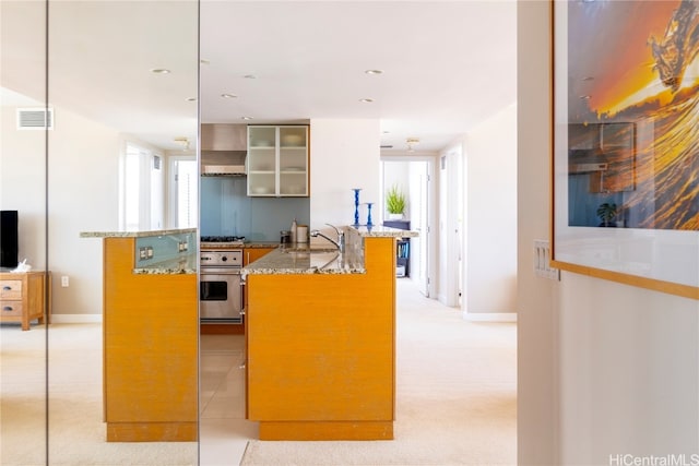 kitchen featuring visible vents, glass insert cabinets, stove, wall chimney range hood, and a sink