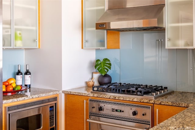 kitchen featuring light stone countertops, wall chimney exhaust hood, and appliances with stainless steel finishes