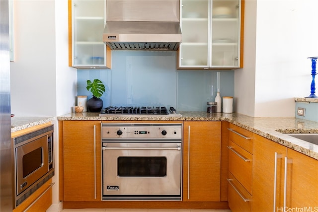 kitchen with wall chimney exhaust hood, light stone countertops, and stainless steel appliances