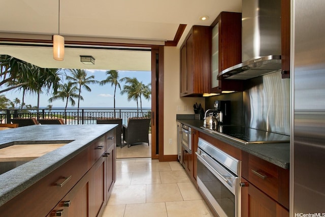 kitchen with black electric cooktop, plenty of natural light, wall chimney exhaust hood, glass insert cabinets, and stainless steel oven