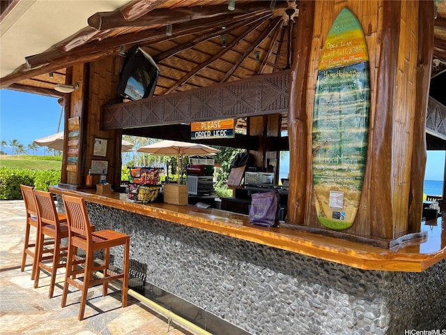 bar featuring stone finish floor and vaulted ceiling with beams