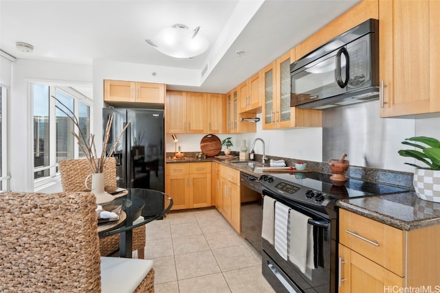 kitchen featuring dark stone counters, light brown cabinetry, light tile patterned floors, and black appliances