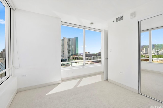 carpeted empty room featuring visible vents, baseboards, and a view of city
