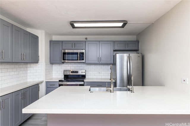 kitchen with appliances with stainless steel finishes, backsplash, gray cabinetry, sink, and hardwood / wood-style flooring