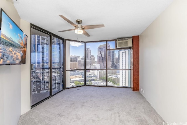 carpeted spare room featuring a wealth of natural light, ceiling fan, a wall mounted air conditioner, and a wall of windows