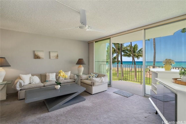 carpeted living room featuring ceiling fan, expansive windows, a water view, and a textured ceiling