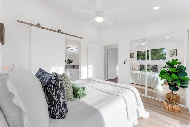 bedroom with ceiling fan, a barn door, light hardwood / wood-style flooring, lofted ceiling, and a closet