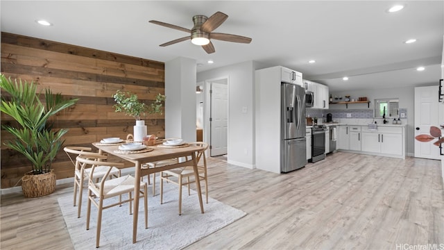 dining area with wooden walls, light wood-type flooring, and ceiling fan