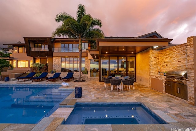 pool at dusk featuring area for grilling, a patio area, and exterior kitchen