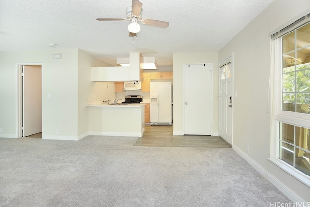 unfurnished living room with a textured ceiling, light colored carpet, sink, and ceiling fan