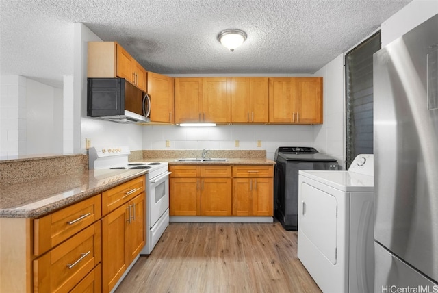 kitchen with sink, white electric stove, washer and dryer, light hardwood / wood-style floors, and stainless steel refrigerator