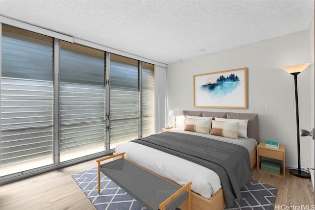 bedroom featuring a wall of windows, a textured ceiling, light wood-type flooring, and access to outside