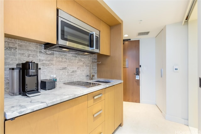 kitchen featuring sink, light stone countertops, cooktop, light brown cabinetry, and tasteful backsplash