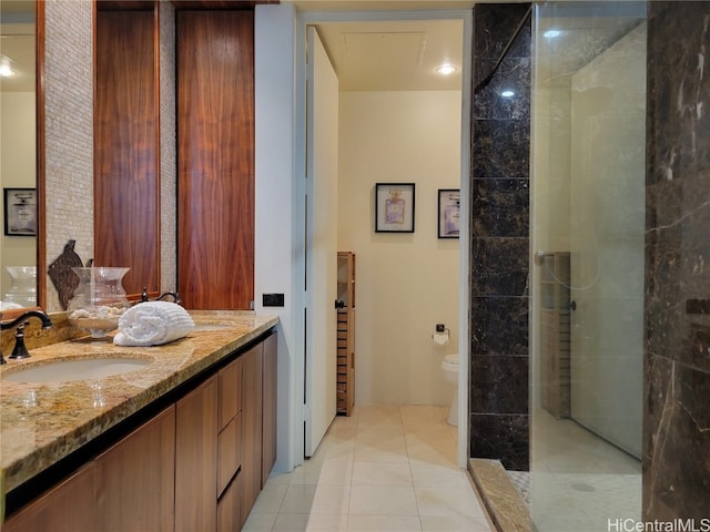 bathroom with toilet, vanity, a tile shower, and tile patterned flooring