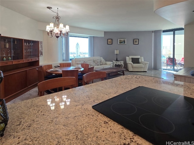 kitchen featuring black electric stovetop, a chandelier, and light stone counters