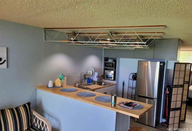 kitchen with kitchen peninsula, a kitchen breakfast bar, a textured ceiling, wood-type flooring, and stainless steel appliances