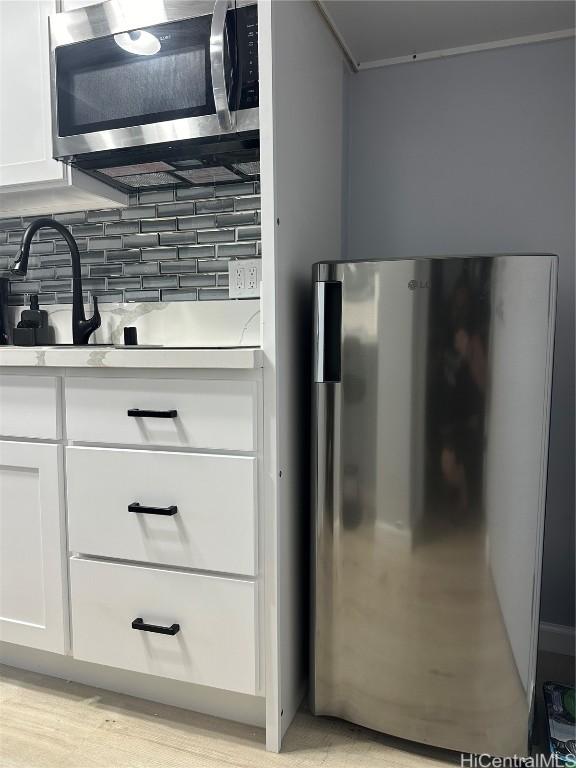 kitchen featuring backsplash, light hardwood / wood-style flooring, white cabinets, and appliances with stainless steel finishes